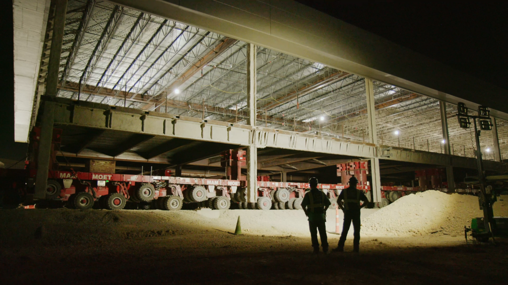 Construction workers watching a large pre-built section of an airport terminal drive by.